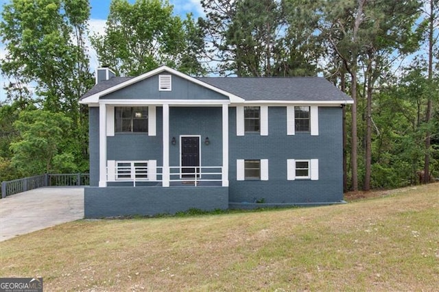 bi-level home featuring a chimney, driveway, brick siding, and a front yard