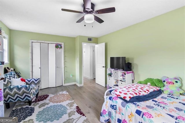 bedroom featuring ceiling fan, visible vents, wood finished floors, baseboards, and a closet