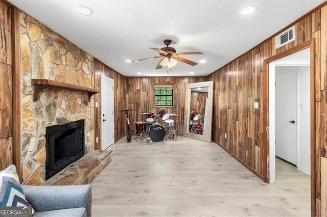 living area with visible vents, ceiling fan, wooden walls, and a stone fireplace