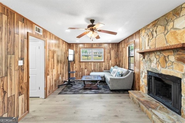 sitting room with a ceiling fan, visible vents, a fireplace, wood walls, and light wood-style floors