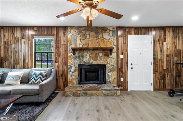 living area featuring wooden walls, a ceiling fan, a stone fireplace, and wood finished floors