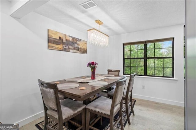 dining space with visible vents, baseboards, light wood-style floors, a textured ceiling, and a chandelier