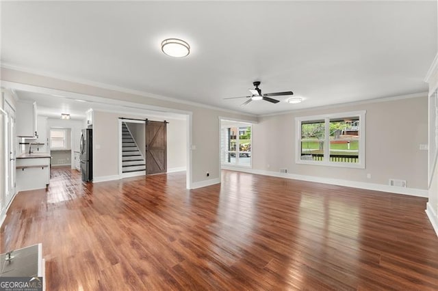 2979 Overwood Ln SW, Snellville, GA 30078 - unfurnished living room with a barn door, ceiling fan, ornamental molding, wood finished floors, and stairs