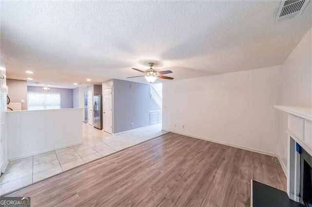 unfurnished living room with light wood finished floors, a fireplace, a textured ceiling, a ceiling fan, and visible vents