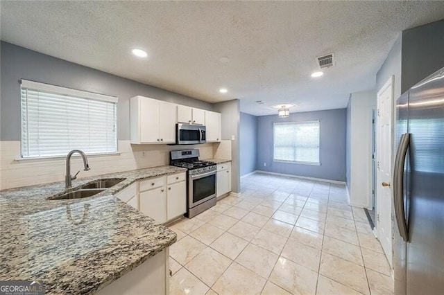 kitchen featuring visible vents, appliances with stainless steel finishes, a sink, light stone counters, and white cabinets