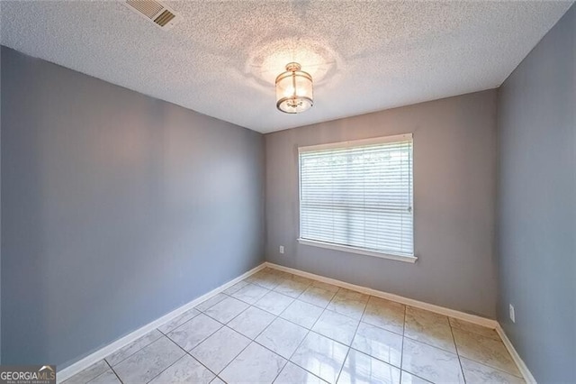 spare room featuring light tile patterned flooring, a textured ceiling, visible vents, and baseboards