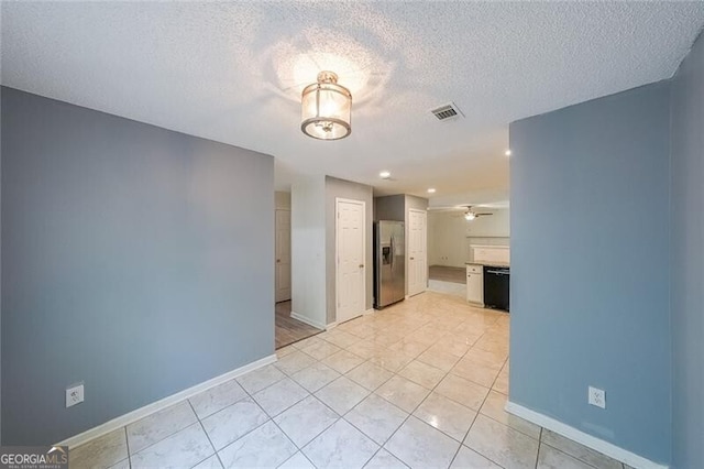 spare room featuring light tile patterned flooring, baseboards, visible vents, and a textured ceiling