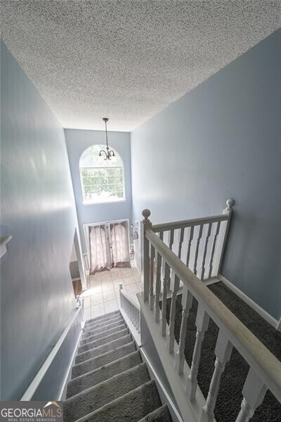 stairway featuring an inviting chandelier and a textured ceiling