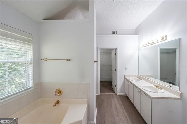full bath with a sink, a garden tub, a textured ceiling, and wood finished floors