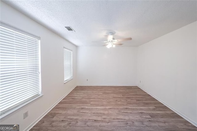 empty room with visible vents, wood finished floors, baseboards, a textured ceiling, and a ceiling fan