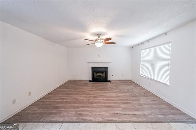 unfurnished living room with wood finished floors, a fireplace, baseboards, a textured ceiling, and a ceiling fan