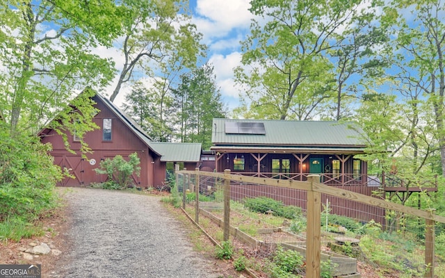 view of front of home with a porch, gravel driveway, a garden, and metal roof
