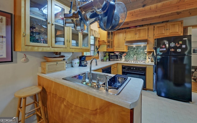 kitchen with light countertops, a peninsula, under cabinet range hood, glass insert cabinets, and black appliances