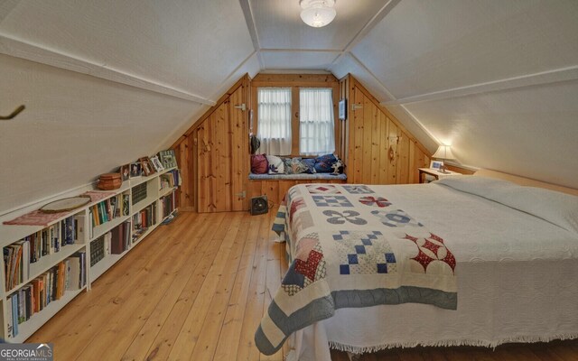 bedroom with wood walls, light wood-style flooring, and vaulted ceiling