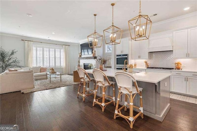 kitchen with open floor plan, gas stovetop, a kitchen island with sink, and premium range hood