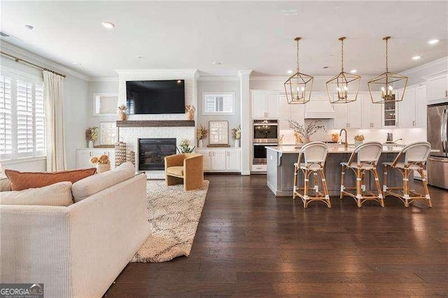 living room featuring dark wood-style flooring, a large fireplace, an inviting chandelier, ornamental molding, and recessed lighting