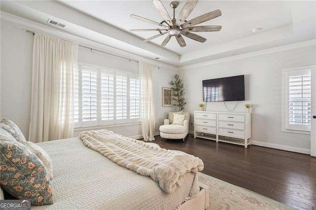 bedroom with a ceiling fan, baseboards, wood finished floors, a tray ceiling, and visible vents