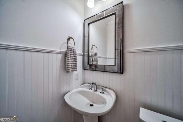 half bathroom featuring toilet, wainscoting, and a sink