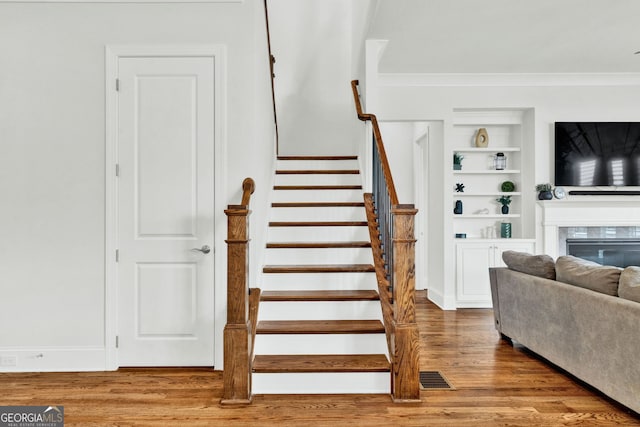 2201 Old Dallas Rd SW, Marietta, GA 30064 - staircase with crown molding, wood finished floors, built in shelves, and a glass covered fireplace