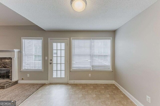 entryway with baseboards, a stone fireplace, and a textured ceiling