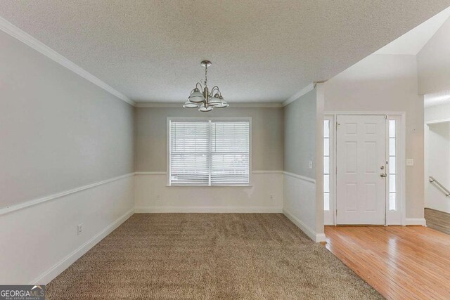 carpeted foyer featuring an inviting chandelier, crown molding, wood finished floors, baseboards, and a textured ceiling