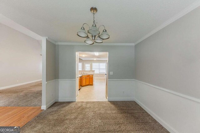 unfurnished dining area with a notable chandelier, light carpet, a textured ceiling, baseboards, and ornamental molding