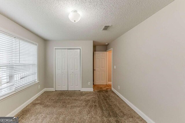 unfurnished bedroom featuring carpet floors, a textured ceiling, baseboards, visible vents, and a closet