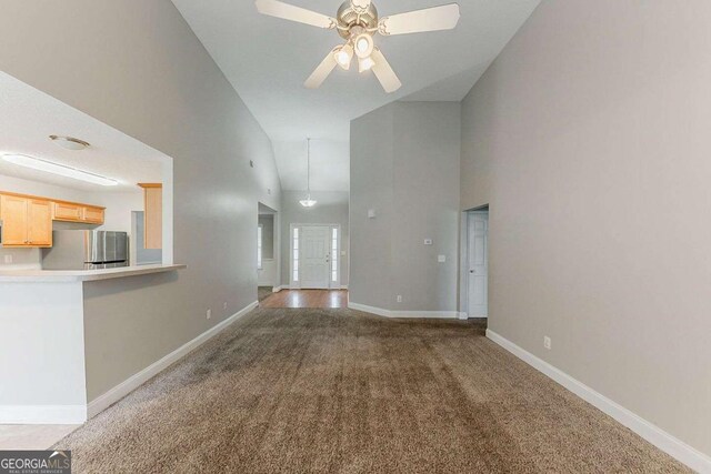 unfurnished living room with a ceiling fan, high vaulted ceiling, baseboards, and carpet