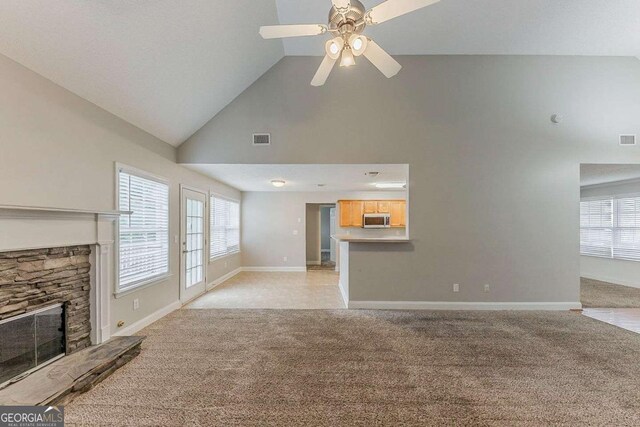 unfurnished living room with high vaulted ceiling, light colored carpet, a stone fireplace, and visible vents