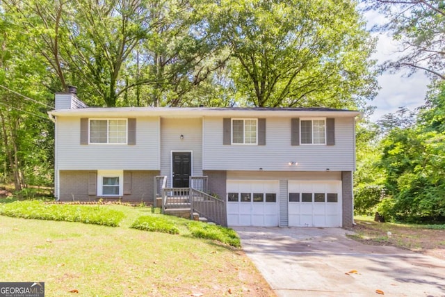 raised ranch with a chimney, a front yard, a garage, brick siding, and concrete driveway
