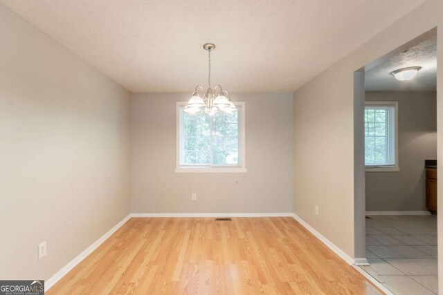 unfurnished room featuring baseboards, an inviting chandelier, and light wood finished floors
