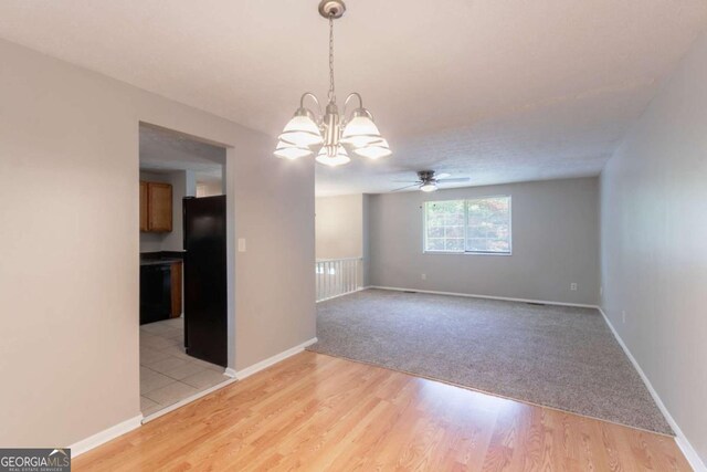 spare room featuring baseboards, light wood-style flooring, ceiling fan with notable chandelier, and light colored carpet
