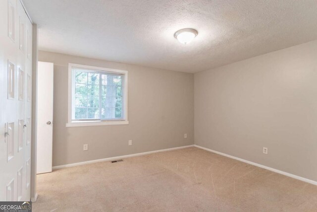 unfurnished bedroom featuring baseboards, light carpet, a textured ceiling, and visible vents
