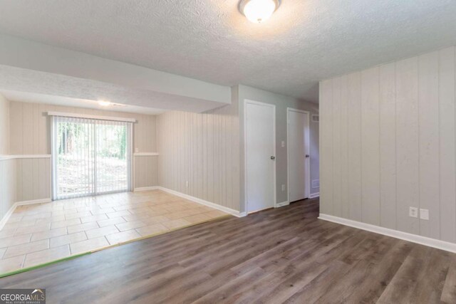 spare room featuring baseboards, wooden walls, a textured ceiling, and wood finished floors