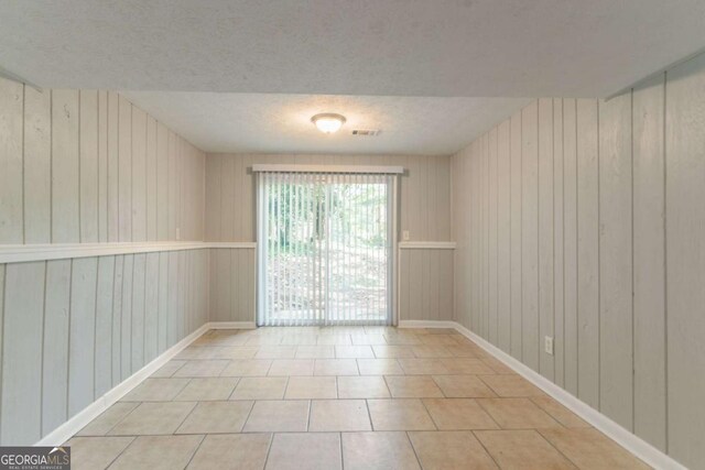 tiled empty room with a textured ceiling, baseboards, wood walls, and visible vents