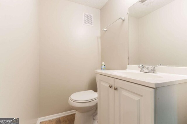 half bath with toilet, tile patterned floors, visible vents, and vanity