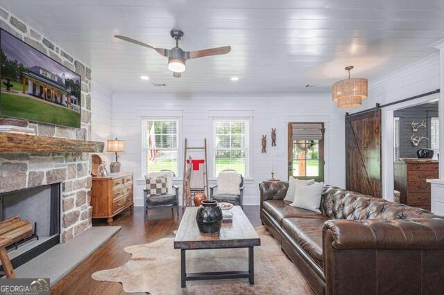 211 Hogan Coweta Rd, Hogansville, GA 30230 - living area featuring a ceiling fan, a stone fireplace, a barn door, and wood finished floors
