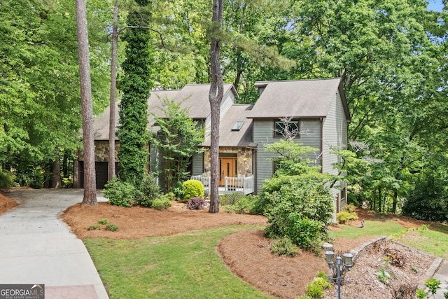 english style home with a porch, driveway, stone siding, and roof with shingles
