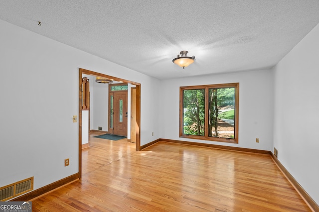 spare room with light wood finished floors, a notable chandelier, a textured ceiling, visible vents, and baseboards