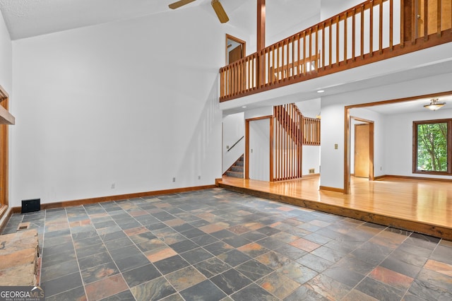 unfurnished living room featuring stairs, stone tile floors, a ceiling fan, a high ceiling, and baseboards