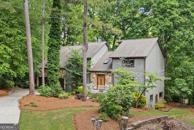 view of front of house featuring driveway, a shingled roof, stone siding, and view of wooded area
