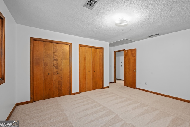 unfurnished bedroom with attic access, two closets, a textured ceiling, carpet floors, and baseboards