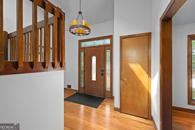 foyer with wood finished floors, visible vents, baseboards, a towering ceiling, and a chandelier