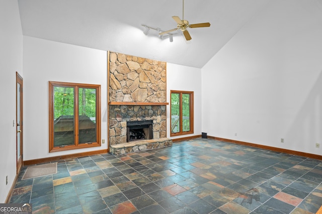 unfurnished living room with high vaulted ceiling, baseboards, stone tile flooring, a fireplace, and a ceiling fan