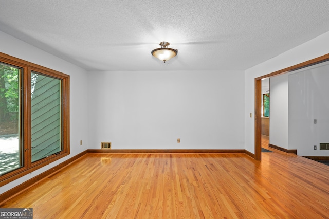 unfurnished room with a textured ceiling, a wealth of natural light, visible vents, and light wood-type flooring
