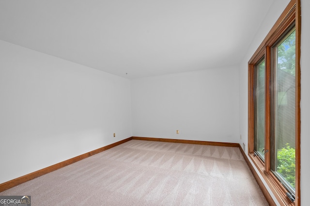unfurnished room featuring healthy amount of natural light, light colored carpet, and baseboards