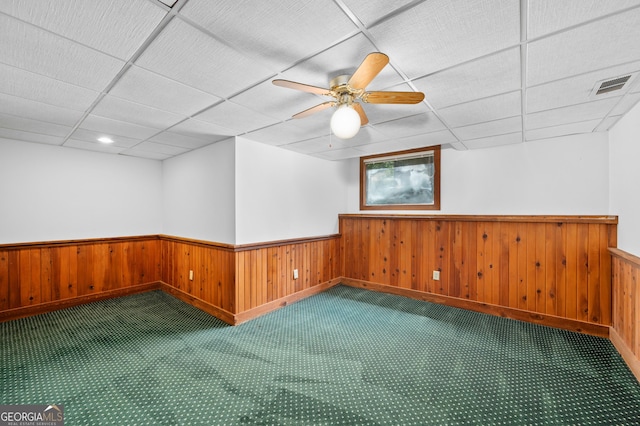 empty room with wainscoting, carpet floors, a paneled ceiling, ceiling fan, and baseboards