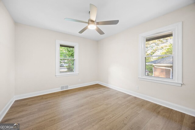 empty room with baseboards, a ceiling fan, wood finished floors, and visible vents