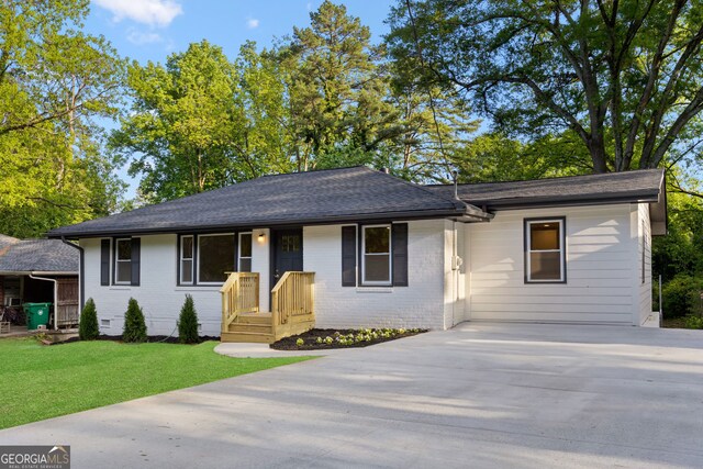 ranch-style home featuring brick siding, driveway, roof with shingles, and a front lawn