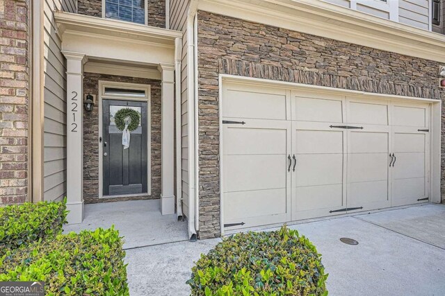 doorway to property featuring an attached garage, concrete driveway, and stone siding